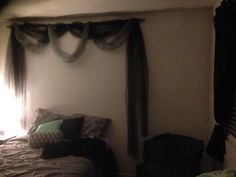 an unmade bed in a dimly lit room with drapes hanging from the ceiling