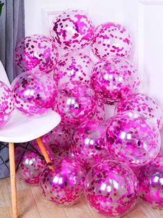 a pile of shiny pink balls sitting on top of a wooden floor next to a white chair