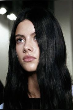 a woman with long black hair and blue eyes looking off to the side in front of a mirror