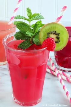 two glasses filled with raspberry and kiwi drink next to strawberries on the table