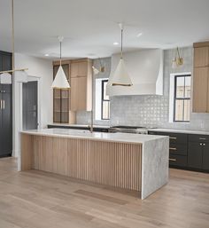 a large kitchen with wooden floors and white counter tops, along with two pendant lights hanging from the ceiling