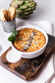 a white bowl filled with food sitting on top of a wooden cutting board next to an artichoke