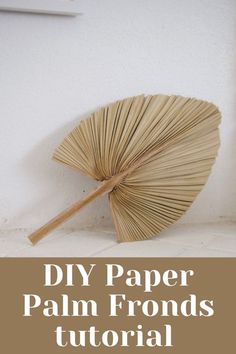 an umbrella made out of paper sitting on top of a white wall with the words diy paper palm fronds