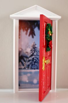 an open red door with christmas decorations on the front and side, in front of a snowy scene