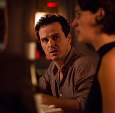 a man and woman sitting at a table talking to each other in a dark room