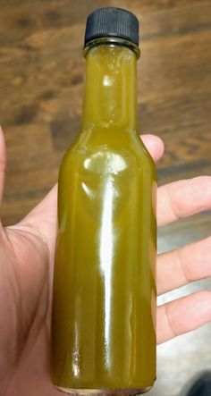 a hand holding a green glass bottle with a black cap on it's top