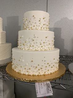 a three tiered white wedding cake with gold dots and pearls on the bottom layer