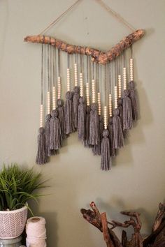 a wall hanging made out of wood sticks and tassels on a white wall next to a potted plant