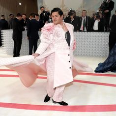 a man in a pink suit and white coat holding a large piece of cloth while standing on a red carpet