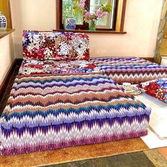 a bed with colorful bedspread and pillows in a room next to a window