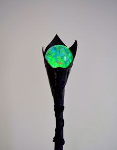 a black umbrella with green and blue designs on it's top is standing in front of a white wall