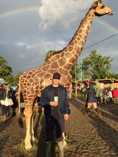 a man standing in front of a giraffe with a rainbow in the background