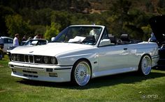 a white bmw convertible parked on top of a lush green field next to other cars