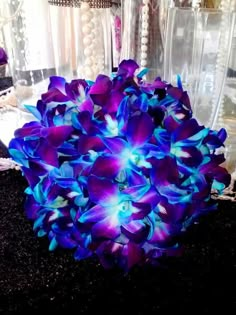 a purple and blue flower sitting on top of a black table next to a mirror