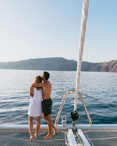 two people standing on the deck of a boat looking out at the water and mountains