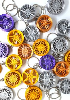 many different colored wheel key chains on a white surface and one is orange, the other is purple