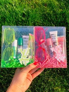 two clear plastic boxes with various items in them on the grass, one being held by a person's hand