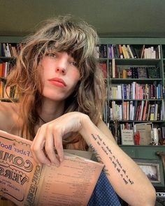 a woman sitting in front of a bookshelf holding a book with writing on it