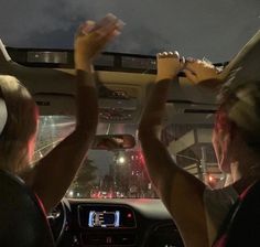 two people sitting in a car with their hands up