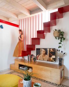 a television sitting on top of a wooden table next to a red stair case in a living room