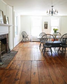 a dining room with wooden floors and chairs around a table in front of a fire place