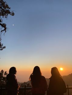 three people are sitting on a bench watching the sun go down in the distance,