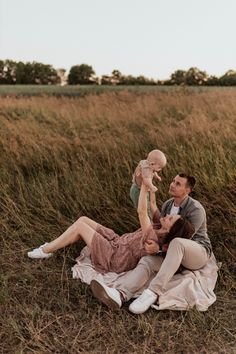 a man, woman and baby are laying on the ground in a field with tall grass