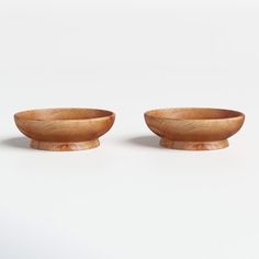 two wooden bowls sitting next to each other on top of a white surface with one bowl in the middle