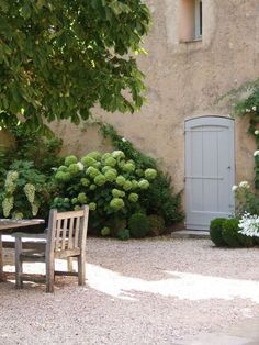 a wooden table sitting in the middle of a garden next to a tall stone building