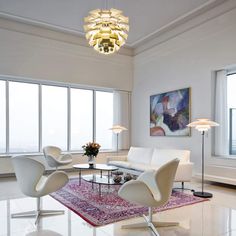 a living room with white furniture and large windows in the backround, along with a rug on the floor