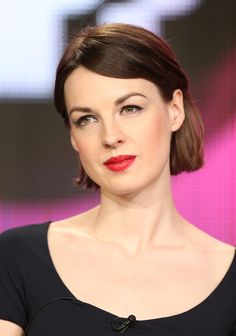 a woman with short hair wearing a black dress and red lipstick on her lips is looking at the camera