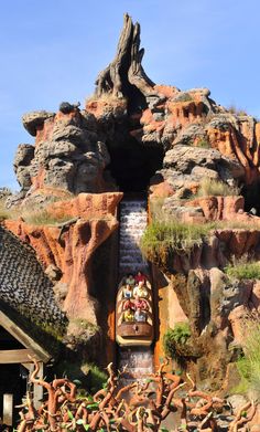 an amusement park ride with people riding on the water slide and trees growing out of it