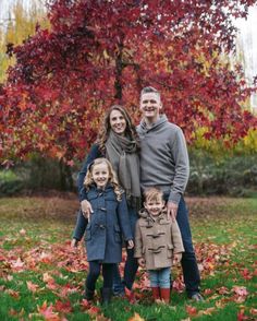 a family standing in front of a tree with fall leaves