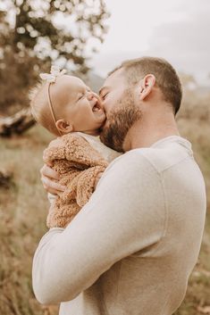 a man holding a baby in his arms and kissing it's face with the other hand