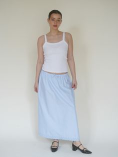 a woman in a white tank top and light blue skirt poses for the camera with her hands on her hips