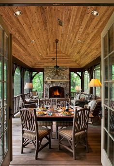 a screen shot of a porch with chairs and a table in the foreground, an open fire place on the far wall