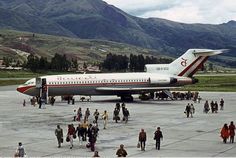 an airplane is parked on the tarmac with people walking around it and mountains in the background