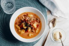 a white bowl filled with pasta and meat soup on top of a blue place mat