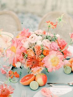 an arrangement of flowers and fruit is sitting on a table with silverware, utensils and napkins