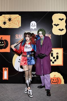 two people dressed up as the joker and harley in front of a halloween themed backdrop