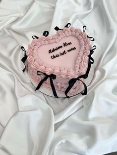 a pink heart shaped cake on top of a white sheet covered tablecloth with black ribbon