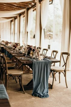 a long table set up with blue linens and place settings for an elegant dinner