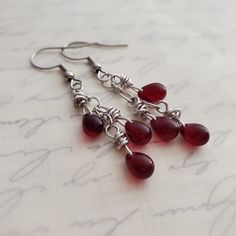 Bloodstone Red Czech Glass Cluster Drop Earrings in Antiqued Silver EARRINGS ONLY Such a rich gothic garnet or bloodstone red! Please note: Bringing them into light draws out the red, otherwise they can almost appear black.  I wrapped garnet Czech glass teardrop beads in titanium wire and minimally suspended three from a length of antiqued silver chain to form a delightful cluster dangle. Earrings fall from your choice earwires.   Earrings can appear almost black in the shadows but light brings out the glorious shades of red.  For clarification, these are not gemstones but Czech glass.  Want a full ensemble?? Add on the pendant in the same bloodstone red/garnet Czech glass as seen in a few of these images. https://www.etsy.com/listing/1157131359/garnet-red-cluster-pendant-necklace REPEAT C Red Teardrop Chandelier Earrings, Red Teardrop Chandelier Earrings With Ear Wire, Red Nickel-free Chandelier Earrings As Gift, Red Wire Wrapped Dangle Earrings, Red Gothic Earrings For Pierced Ears, Red Wire Wrapped Metal Earrings, Gothic Red Nickel-free Earrings, Antique Silver Earrings, Earrings Fall