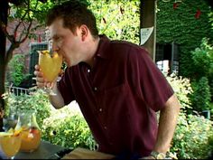 a man drinking from a wine glass in front of a table with fruit on it