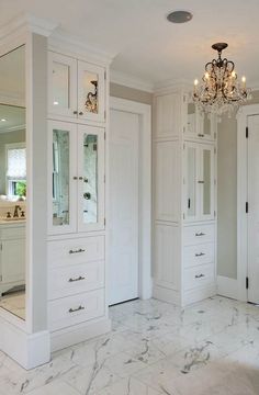 a large bathroom with marble floors and white cabinetry, chandelier and mirror