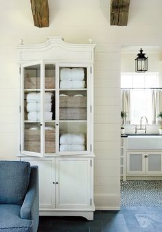 a white china cabinet with towels in it and a blue chair next to the sink