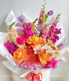 a bouquet of colorful flowers in a white vase with a red ribbon tied around it