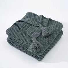 two gray crocheted blankets folded on top of each other with tassels