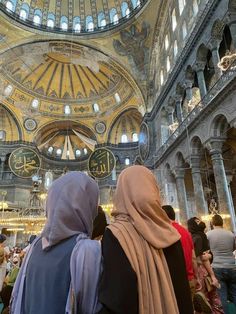 two women in headscarves looking up at the ceiling inside an ornately decorated building