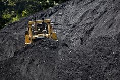 a yellow bulldozer is sitting on top of a pile of black dirt in the woods